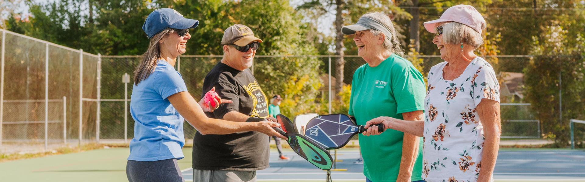 group of four pickleball players tapping paddles over the net at an outdoor court in Tiny on a sunny day