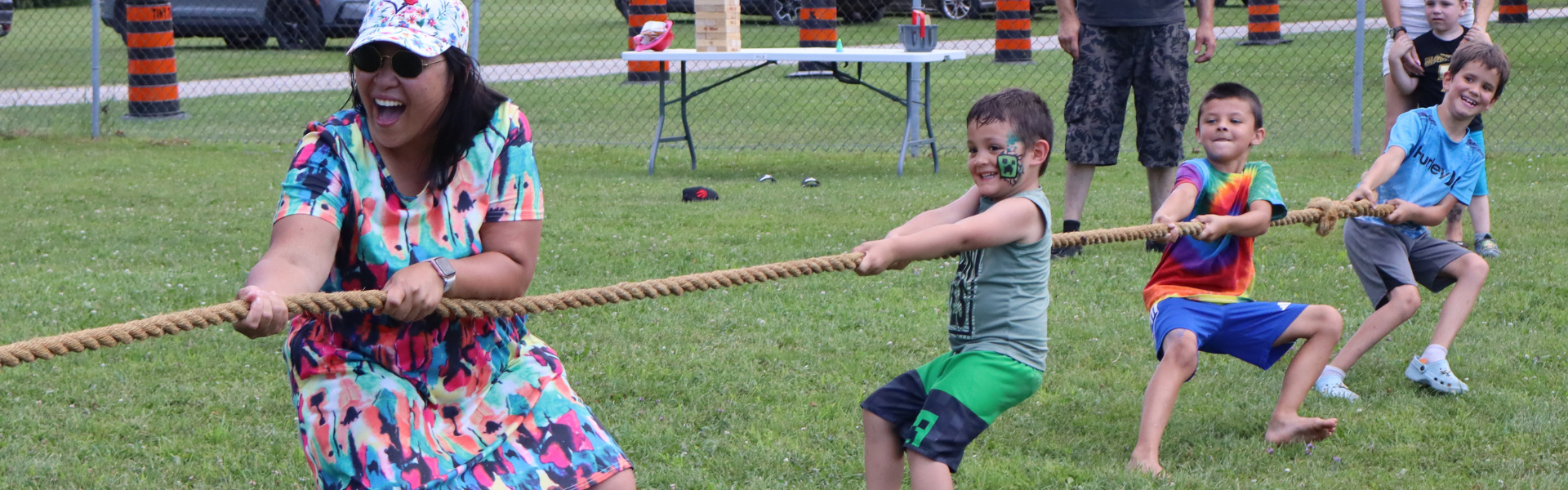 A woman and 3 kids pulling a rope during tug of war.