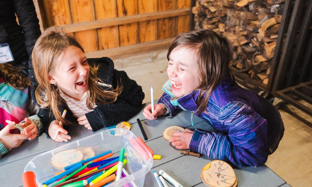 Two campers colouring and laughing at a table