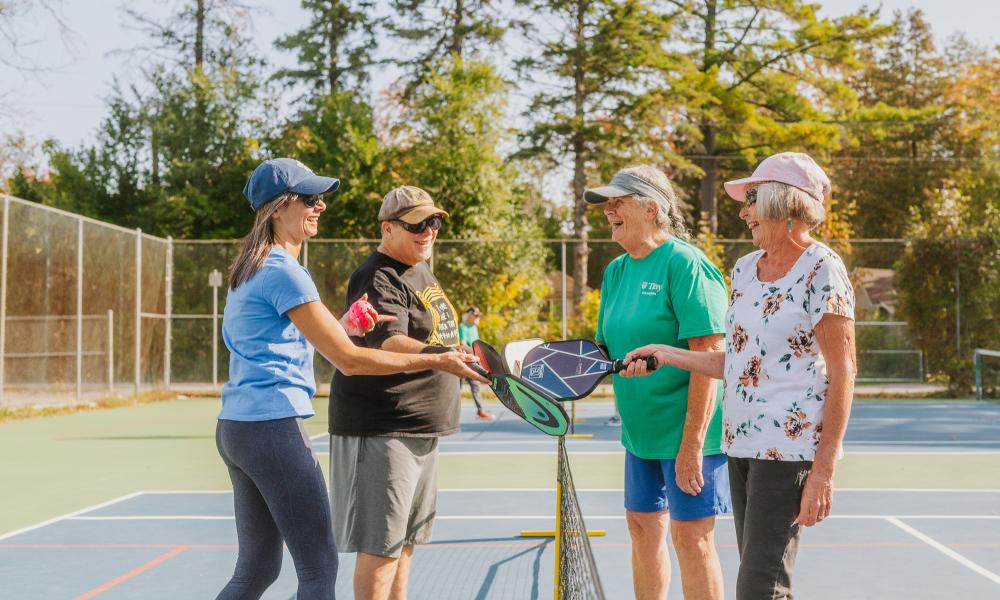 group of four pickleball players tapping paddles over the net at an outdoor court in Tiny on a sunny day