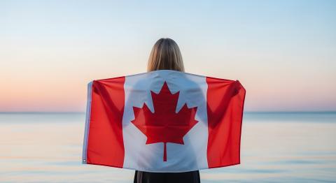 Person standing facing the beach with a canada flag across their back