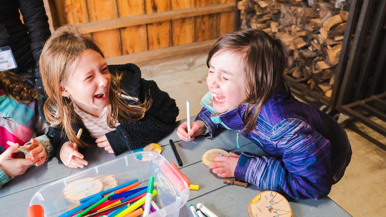 two girls laughing while sitting at a table doing a craft activity at a Tiny camp