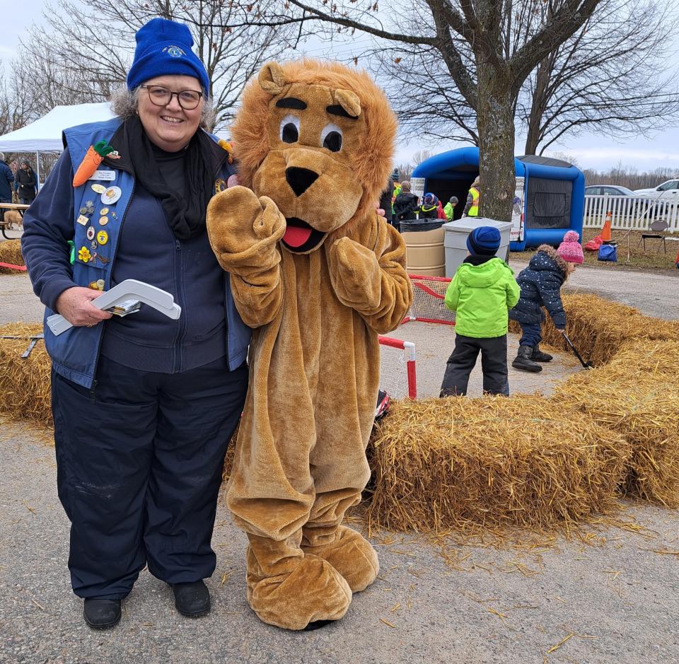 Lions Club member with the lion mascot in front of the mini hockey stick arena