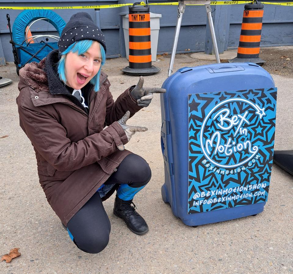 Bex in Motion performer squatting down to show off their branded suitcase that holds props for their fire performance