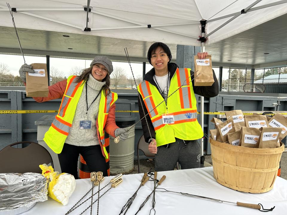 Two volunteers posing with the smores-making goodie bags and marshmallow roasting sticks with the pavilion in the background