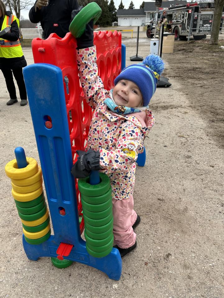 Young girl smiling and reaching up to place one of the Connect 4 rings into the top slot