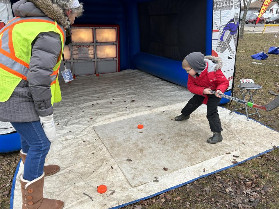 Young child taking slapshots with a hockey stick and puck with a volunteer cheering them on