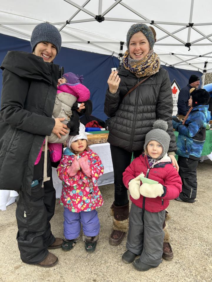 Two moms with their young children enjoying maple syrup samples