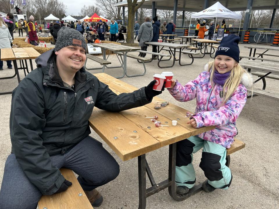 Father and daughter sitting at a picnic bench toasting with hot chocolate