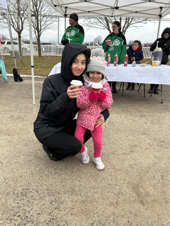 Mom bending down to pose with young daughter - both enjoying a hot chocolate