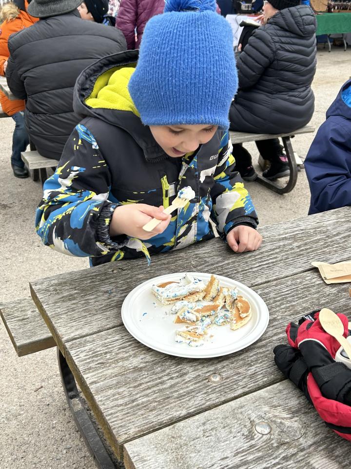 young boy enjoying their pancakes and whipped cream at a picnic table