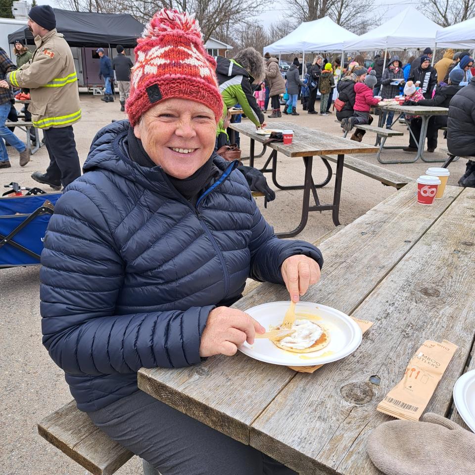 Woman enjoying pancakes sitting at a picnic bench with other attendees in the background