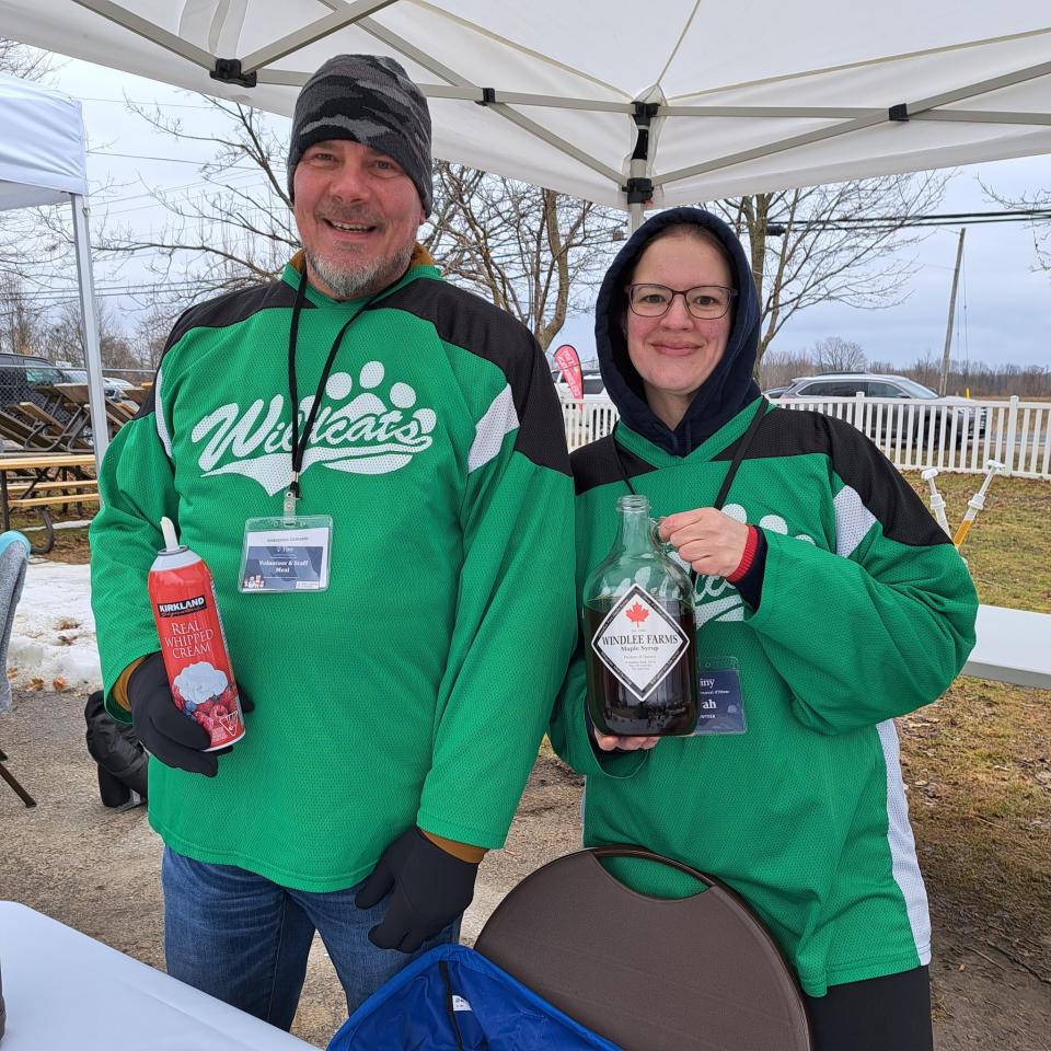 Two volunteers wearing green jerseys posing with pancake toppings at one of the booths