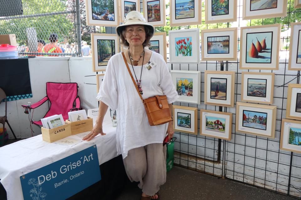 Deb Grise Art Booth featuring many paintings behind the woman posing