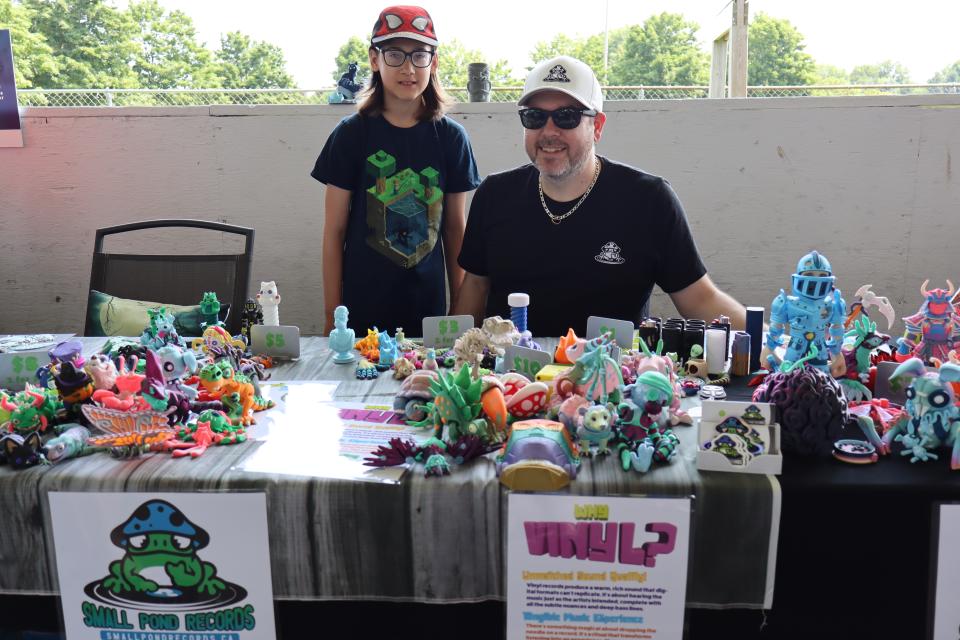 Father and son sitting behind their Small Pond Records booth with a collection of critters, action figures, and toys on the table