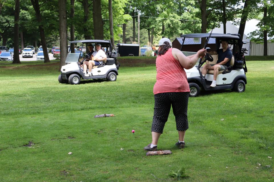 Female golfer mid swing with golf carts parked in the background