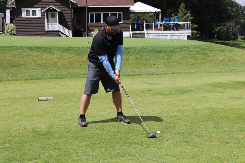 Male golfer lining up their swing at the closest to the line challenge with the clubhouse in the background