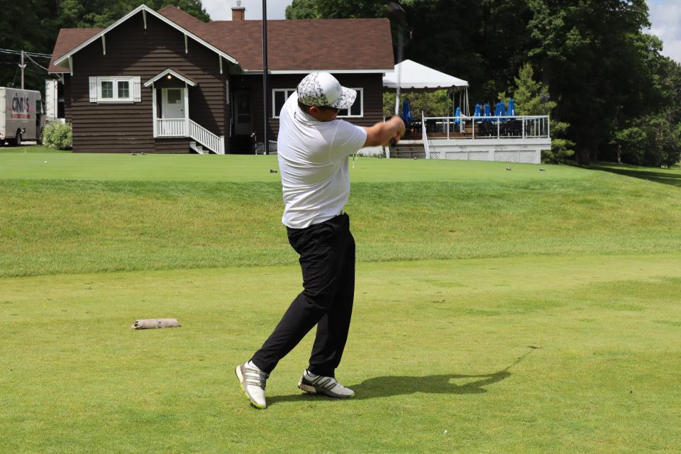 Male golfer mid-swing at the closest to the line challenge with the clubhouse in the background