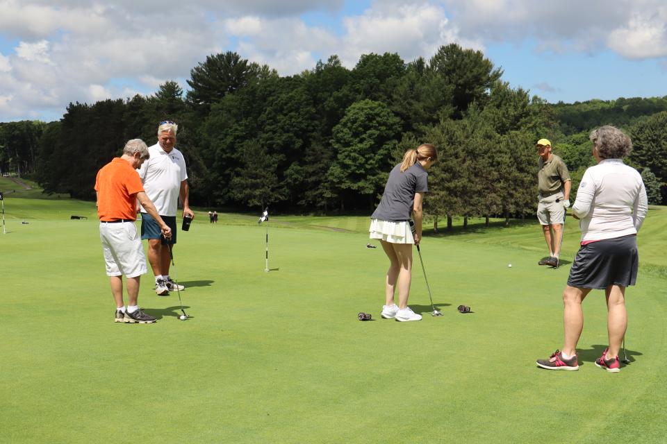 Mixed golf foursome and Mayor Evans onlooking one of the women in the Mayor's putting challenge