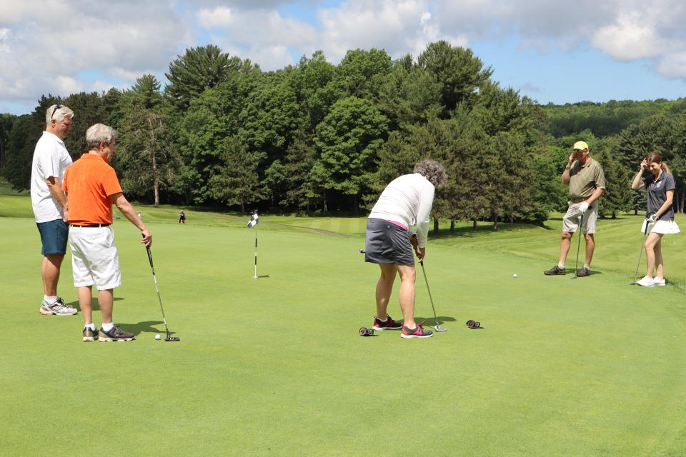 Mixed golf foursome and Mayor Evans onlooking one of the women in the Mayor's putting challenge