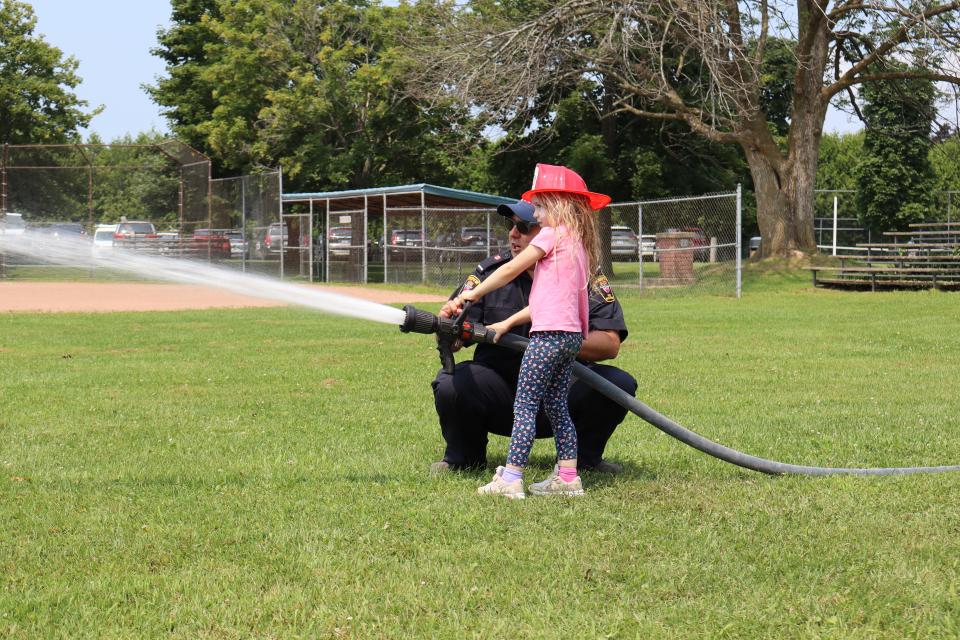 Image of a young girl and a firefighter using the fire hose