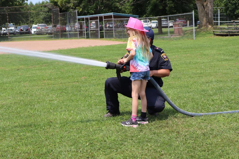 Image of a young girl in and a firefighter using the fire hose