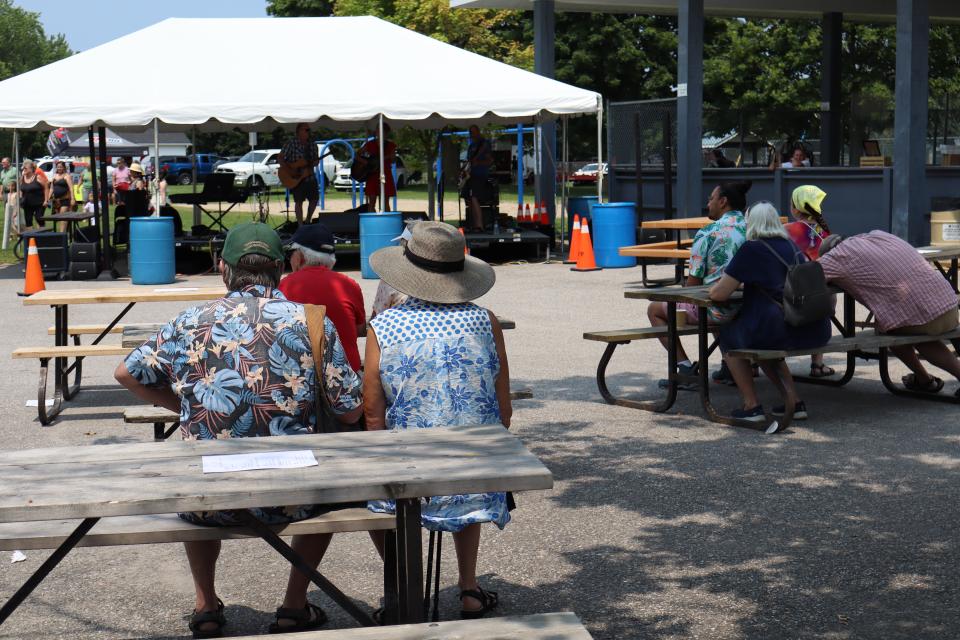 Image showing several people sitting on picnic tables watching the Karla Crawford Band under the tent