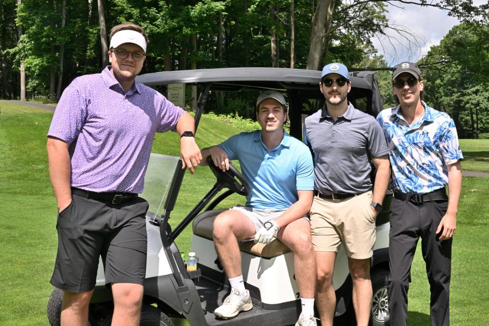 Men's golf foursome out on the greens, sitting and leaning on one of their carts