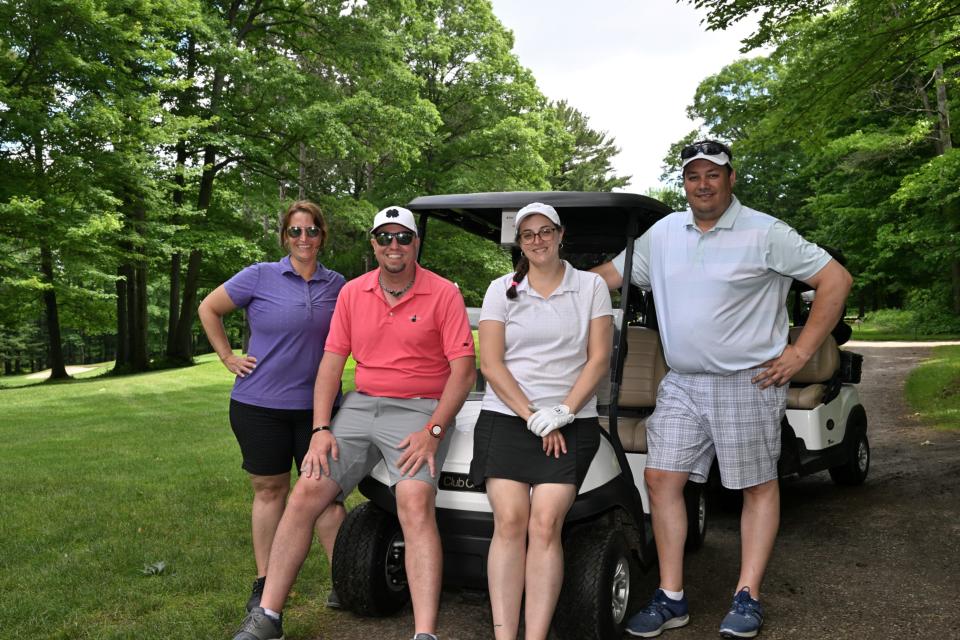 Mixed golf foursome out on the greens sitting and leaning on the back of their golf cart