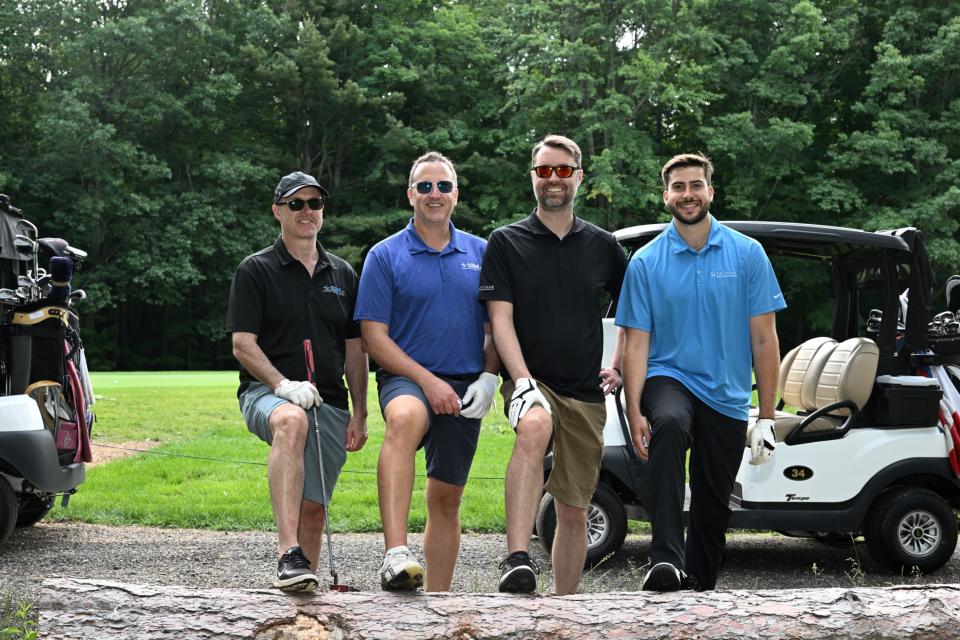 Men's golf foursome posing with one foot elevated on a log with their golf carts behind them