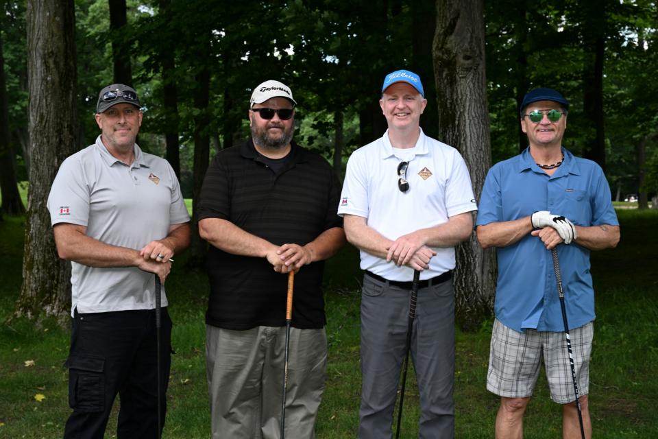 Men's golf foursome all posing with their golf clubs resting on the ground