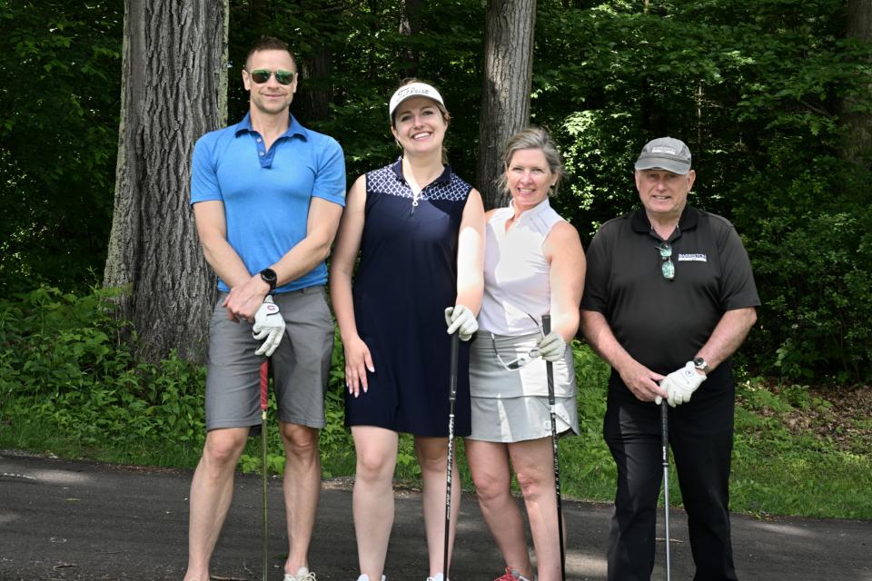 Mixed golf foursome posing with their clubs resting on the ground along a pathway