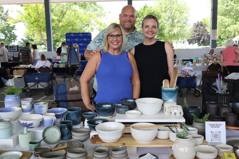 Team of 3 - a man and two women behind their pottery table at the vendor fair