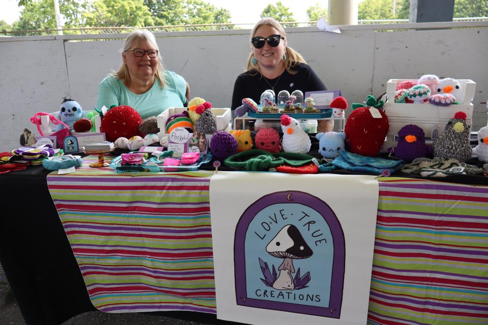 Two women sitting behind their Love True Creations table with a collection of knitted and hand made goods