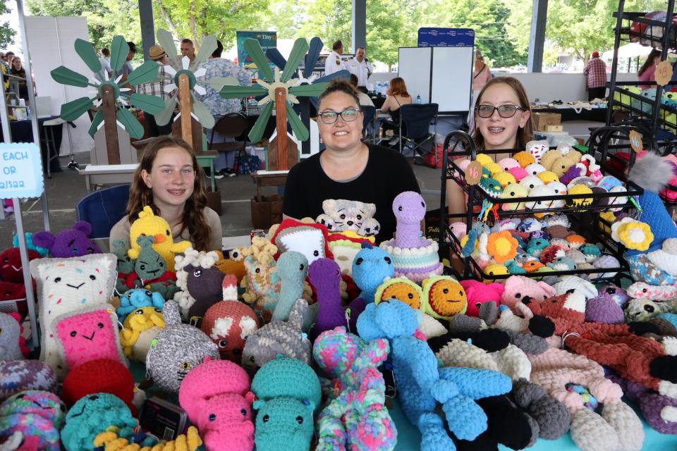 Woman and two young girls sitting in their booth featuring a collection of knitted stuffed animals and critters