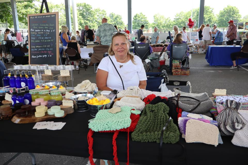 Woman sitting behind their artisal booth with soaps, sprays, and knitted goods