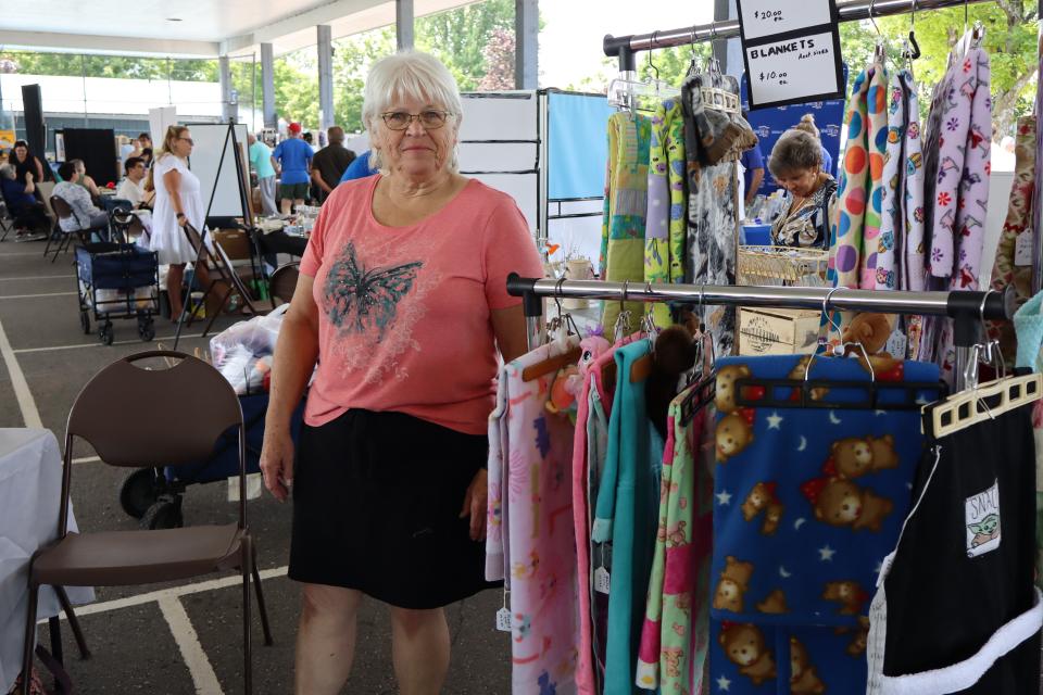 Woman standing in their booth with many blankets in fun colours and patterns