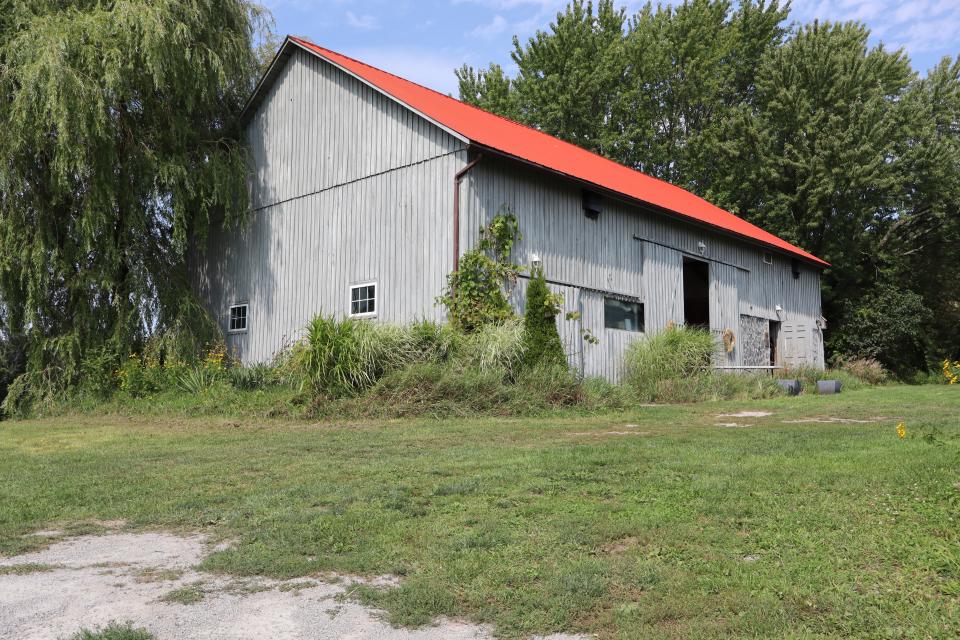 Grey coloured barn with a bright red roof with large trees overhanging the barn's roof