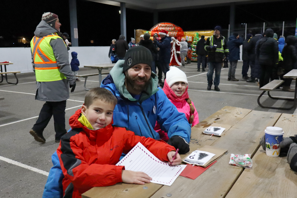 young father with their two children writing letters to santa at a picnic table in the Perkinsfield Pavilion 