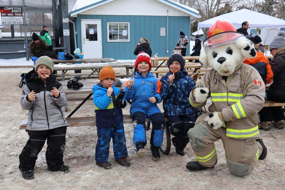 four young boys sitting on a picnic bench enjoying maple taffy with Sparky the dog