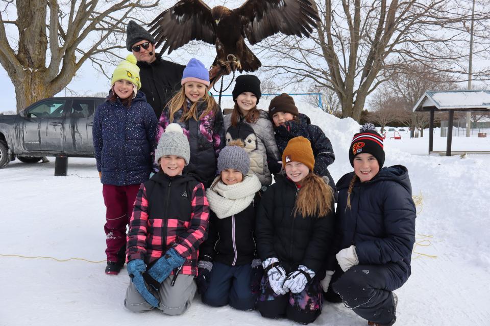 group of children posing with a raptor bird that has their wings open and their handler