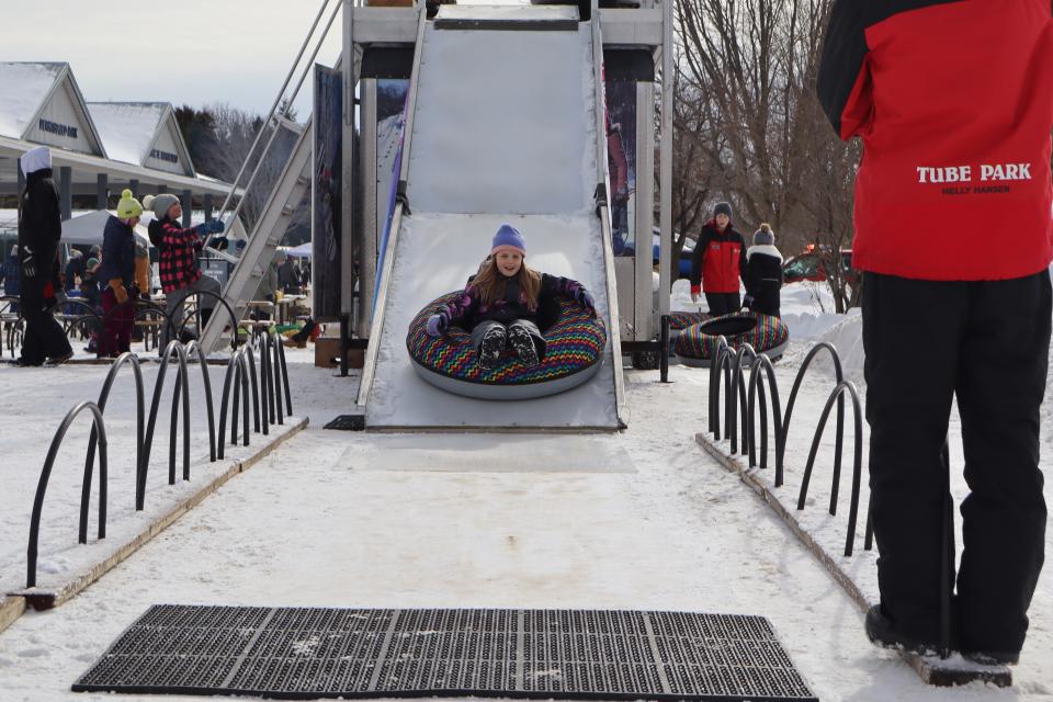 young girl tubing down the mobile snow hill with Snow Valley staff in the background