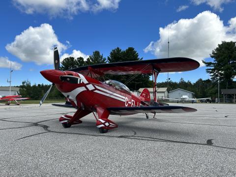 image of small hobby airplane that is mostly red in colour with white highlights on the tarmac at the Huronia Airport on a bright day with some fluffy white clouds in the sky